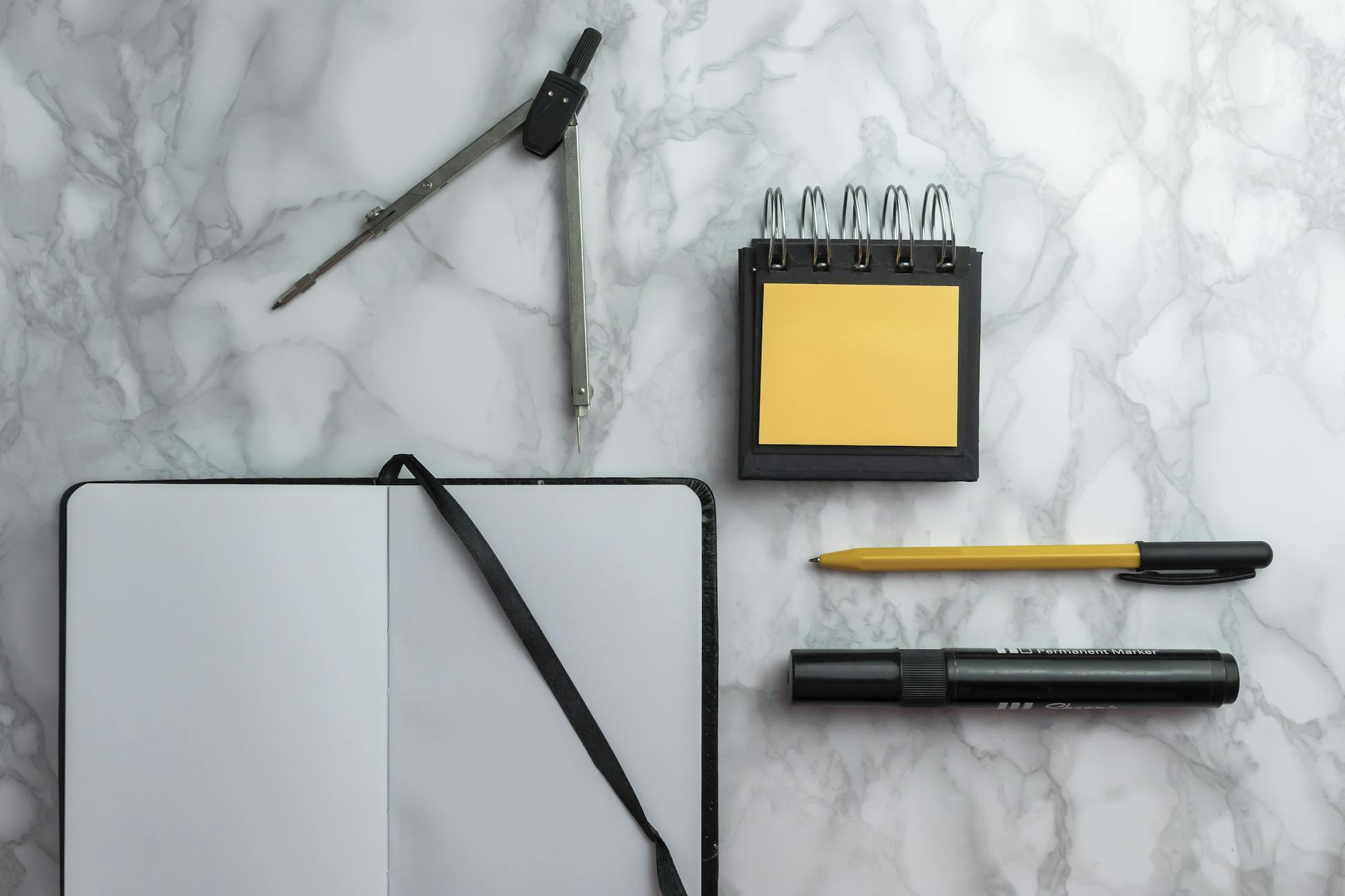 Flat lay of school supplies including compass, notebook, pen, and sticky notes on a marble surface.